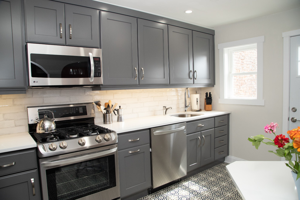Photo of a small classic l-shaped kitchen in Philadelphia with a single-bowl sink, shaker cabinets, grey cabinets, engineered stone countertops, white splashback, ceramic splashback, stainless steel appliances, ceramic flooring and white worktops.
