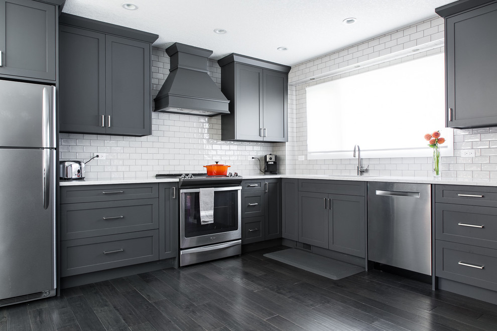 Modern inredning av ett stort kök, med en undermonterad diskho, skåp i shakerstil, grå skåp, marmorbänkskiva, gult stänkskydd, stänkskydd i tunnelbanekakel, rostfria vitvaror, mörkt trägolv, en halv köksö och svart golv