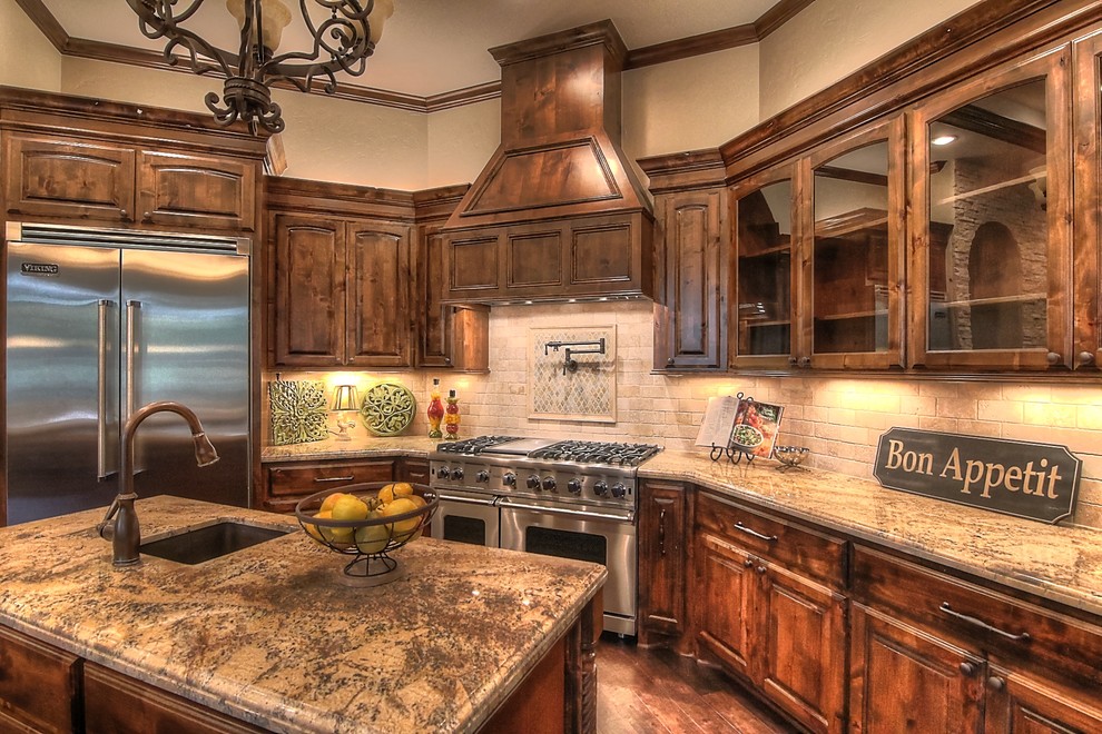 Large tuscan l-shaped dark wood floor eat-in kitchen photo in Houston with an undermount sink, raised-panel cabinets, dark wood cabinets, granite countertops, beige backsplash, stone tile backsplash, stainless steel appliances and an island