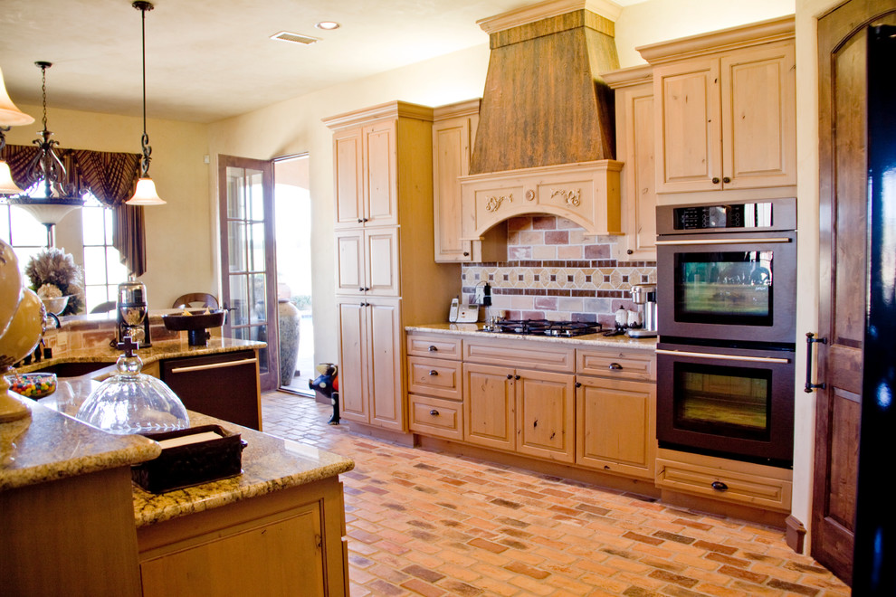 Mediterrane Wohnküche mit profilierten Schrankfronten, hellen Holzschränken, Granit-Arbeitsplatte, Küchenrückwand in Beige, Rückwand aus Steinfliesen, Backsteinboden und Kücheninsel in Austin