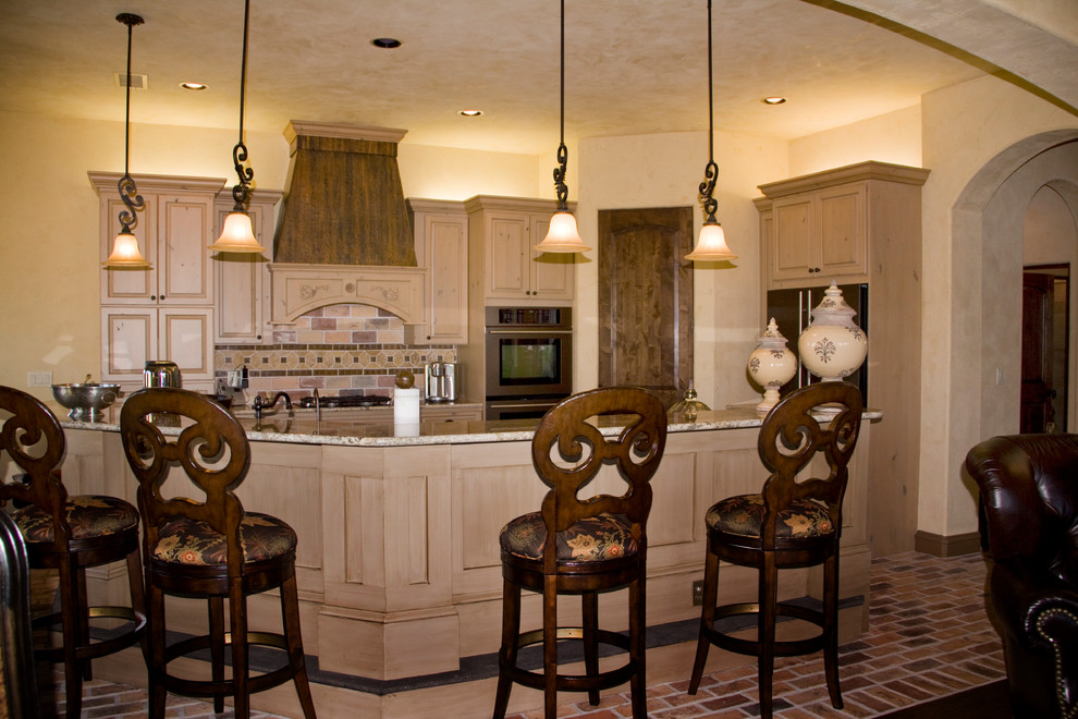 Inspiration for a mediterranean kitchen/diner in Austin with raised-panel cabinets, light wood cabinets, granite worktops, beige splashback, stone tiled splashback, brick flooring and an island.