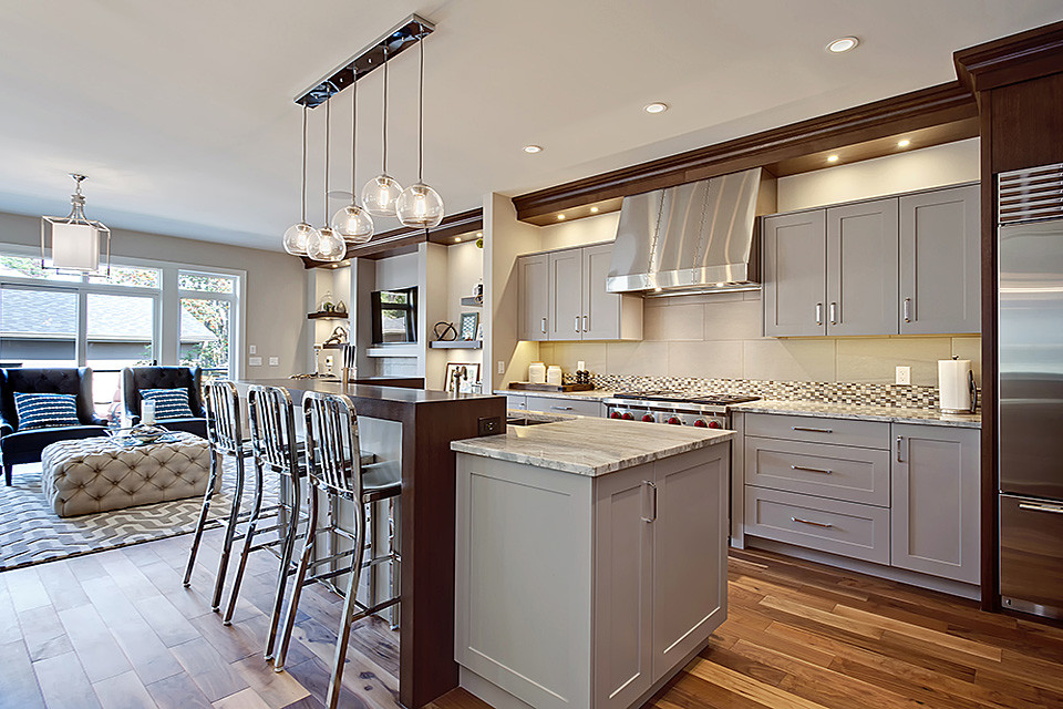Cette photo montre une cuisine tendance avec un placard à porte shaker, des portes de placard grises, un électroménager en acier inoxydable, parquet clair et îlot.