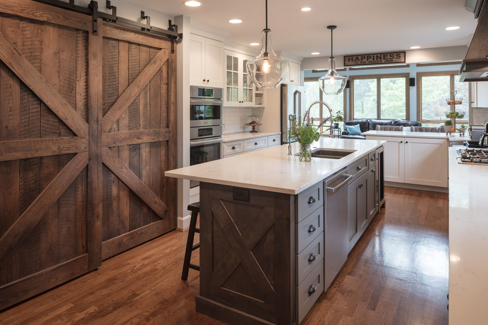 Design ideas for a medium sized rustic u-shaped kitchen/diner in Cincinnati with a submerged sink, shaker cabinets, white cabinets, engineered stone countertops, white splashback, metro tiled splashback, stainless steel appliances, medium hardwood flooring, an island and brown floors.