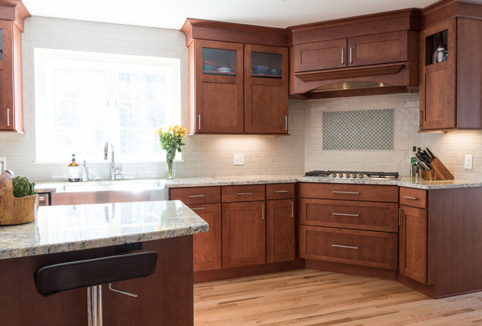 Klassisk inredning av ett mellanstort beige beige kök, med en rustik diskho, skåp i shakerstil, skåp i mellenmörkt trä, granitbänkskiva, grått stänkskydd, stänkskydd i tunnelbanekakel, rostfria vitvaror, mellanmörkt trägolv, en köksö och brunt golv