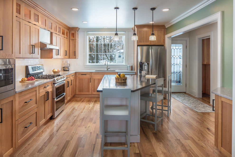 Inredning av ett klassiskt grå grått l-kök, med en undermonterad diskho, skåp i shakerstil, skåp i mellenmörkt trä, vitt stänkskydd, stänkskydd i tunnelbanekakel, rostfria vitvaror, mellanmörkt trägolv, en köksö och brunt golv