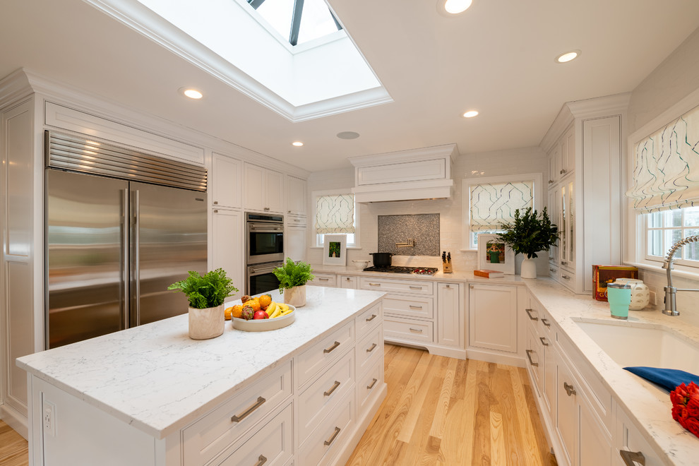 Exempel på ett avskilt, mellanstort klassiskt vit vitt u-kök, med en undermonterad diskho, luckor med profilerade fronter, vita skåp, bänkskiva i kvarts, vitt stänkskydd, stänkskydd i glaskakel, rostfria vitvaror, ljust trägolv, en köksö och beiget golv