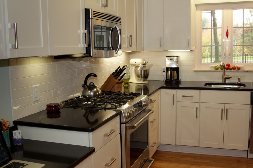 Foto på ett funkis kök, med en undermonterad diskho, skåp i shakerstil, vita skåp, granitbänkskiva, vitt stänkskydd, stänkskydd i tunnelbanekakel och rostfria vitvaror
