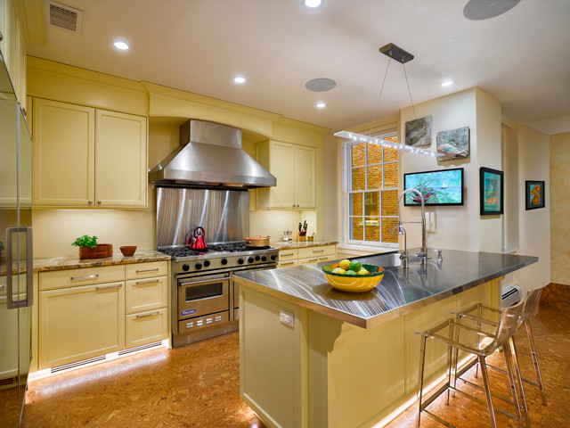 Klassisk inredning av ett mellanstort flerfärgad flerfärgat kök, med en integrerad diskho, luckor med infälld panel, gula skåp, bänkskiva i rostfritt stål, gult stänkskydd, glaspanel som stänkskydd, rostfria vitvaror, korkgolv, en köksö och brunt golv