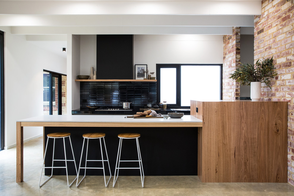 Immagine di un'ampia cucina parallela design con top in superficie solida, paraspruzzi nero, pavimento in cemento, pavimento grigio, top bianco, ante nere e penisola