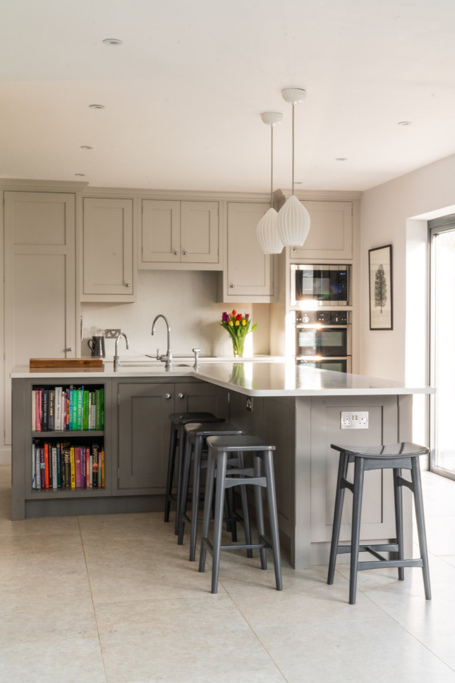 Photo of a large traditional l-shaped kitchen/diner in Surrey with shaker cabinets, grey cabinets, quartz worktops, white splashback, stainless steel appliances, an island, grey floors and white worktops.