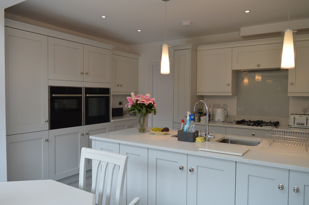 Foto på ett stort funkis vit kök, med en undermonterad diskho, skåp i shakerstil, vita skåp, bänkskiva i kvartsit, glaspanel som stänkskydd, rostfria vitvaror, mellanmörkt trägolv, en köksö och grått golv