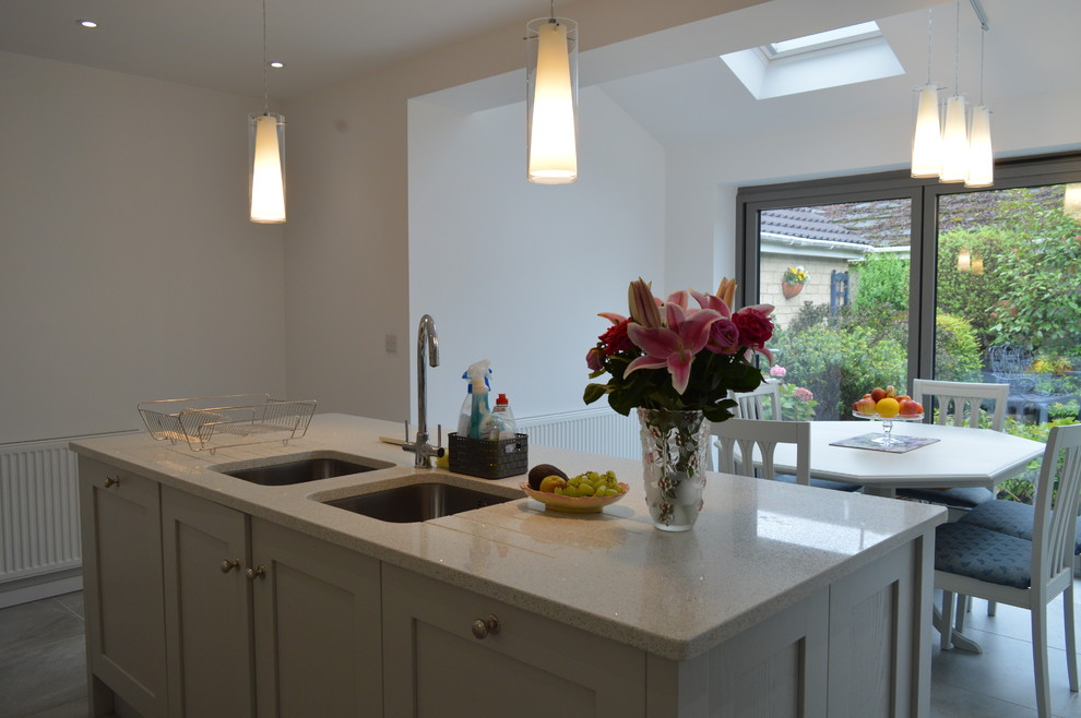 Photo of a large contemporary l-shaped open plan kitchen in Other with a submerged sink, shaker cabinets, white cabinets, quartz worktops, glass sheet splashback, stainless steel appliances, medium hardwood flooring, an island, grey floors and white worktops.