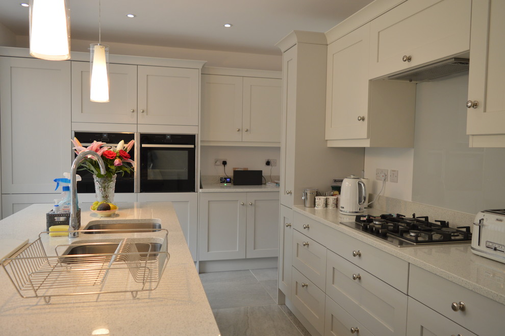 Exempel på ett stort modernt vit vitt kök, med en undermonterad diskho, skåp i shakerstil, vita skåp, bänkskiva i kvartsit, glaspanel som stänkskydd, rostfria vitvaror, mellanmörkt trägolv, en köksö och grått golv