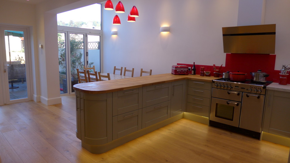Photo of a medium sized contemporary u-shaped open plan kitchen in Other with a belfast sink, shaker cabinets, green cabinets, wood worktops, red splashback, glass sheet splashback, stainless steel appliances and medium hardwood flooring.