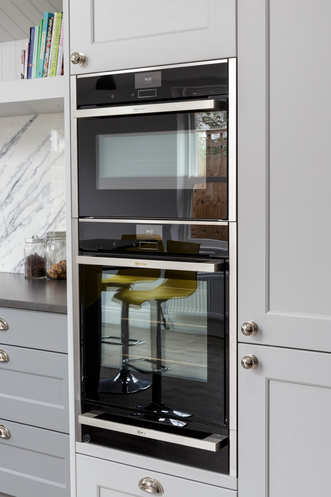 Exemple d'une cuisine ouverte chic avec un placard à porte shaker, des portes de placard grises, un plan de travail en quartz, une crédence en marbre, un électroménager noir, îlot et une crédence blanche.