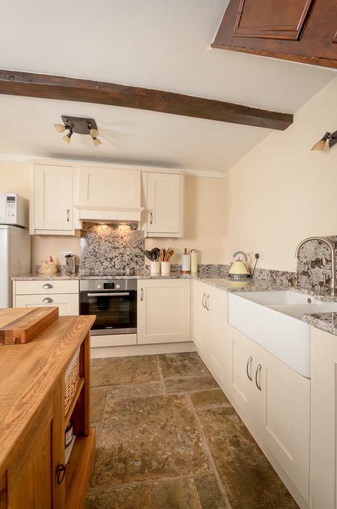 Mittelgroße Urige Küche mit Landhausspüle, weißen Schränken, Granit-Arbeitsplatte, Küchenrückwand in Grau und Küchengeräten aus Edelstahl in Sonstige