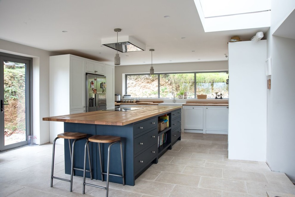 Inspiration for a large classic u-shaped kitchen/diner in Gloucestershire with a double-bowl sink, shaker cabinets, blue cabinets, wood worktops, stainless steel appliances, travertine flooring, an island, beige floors and brown worktops.