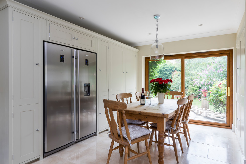 Photo of a large country u-shaped kitchen/diner in London with a belfast sink, shaker cabinets, grey cabinets, quartz worktops, white splashback, ceramic splashback, stainless steel appliances, limestone flooring, an island and beige floors.