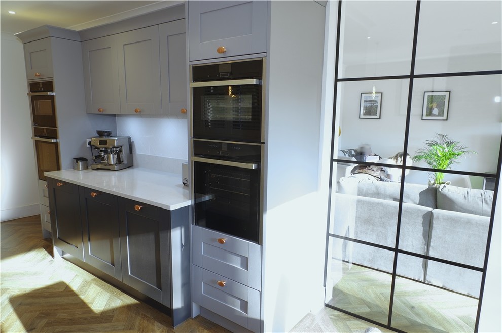 Idee per una cucina moderna con ante grigie, top in quarzite, paraspruzzi bianco, elettrodomestici neri, pavimento marrone e top grigio