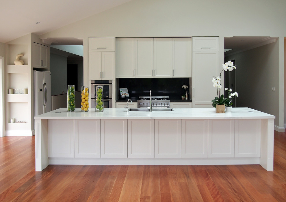 Inspiration for a large traditional galley kitchen/diner in Sydney with a belfast sink, shaker cabinets, white cabinets, engineered stone countertops, grey splashback, stone slab splashback, stainless steel appliances, medium hardwood flooring and multiple islands.