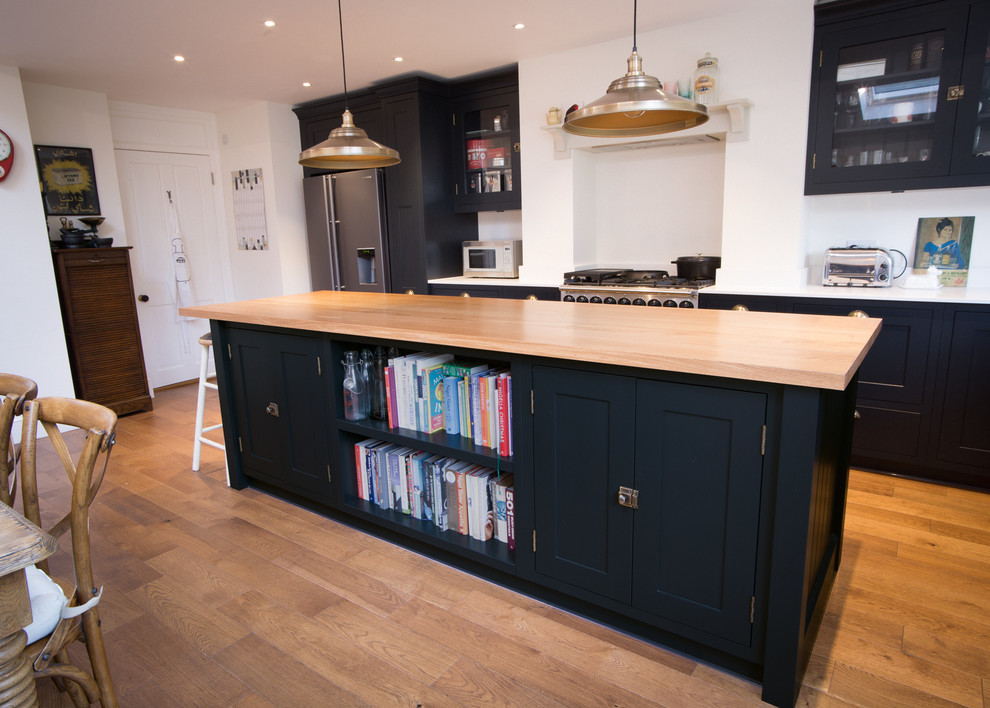 Photo of a medium sized traditional l-shaped kitchen/diner in London with a built-in sink, recessed-panel cabinets, black cabinets, composite countertops, white splashback, stone slab splashback, stainless steel appliances, medium hardwood flooring and an island.