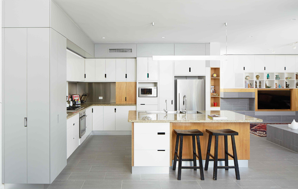 Exempel på ett minimalistiskt kök, med släta luckor, vita skåp, rostfria vitvaror, en köksö, en dubbel diskho, granitbänkskiva, stänkskydd med metallisk yta, stänkskydd i metallkakel, klinkergolv i keramik och grått golv