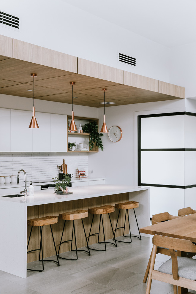 Design ideas for a large contemporary galley kitchen/diner in Other with a submerged sink, flat-panel cabinets, white cabinets, white splashback, matchstick tiled splashback, an island, grey floors and white worktops.