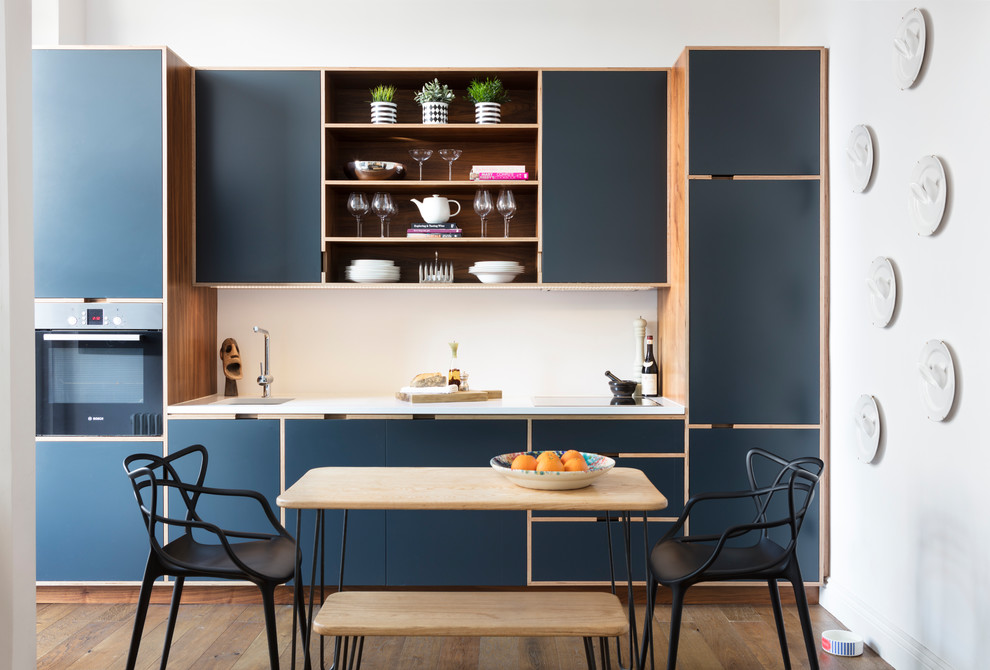 Inredning av ett minimalistiskt vit linjärt vitt kök och matrum, med en undermonterad diskho, släta luckor, blå skåp, vitt stänkskydd, mellanmörkt trägolv och brunt golv