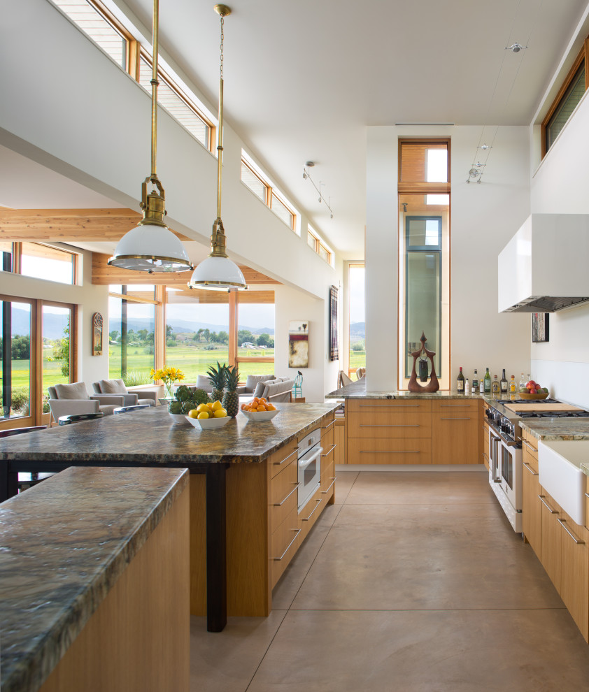 Expansive country open plan kitchen in Denver with a belfast sink, flat-panel cabinets, light wood cabinets, granite worktops, white splashback, glass sheet splashback, stainless steel appliances, concrete flooring, an island and grey floors.