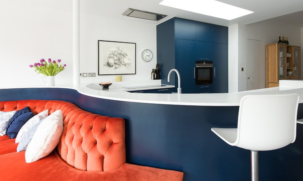 ロンドンにある高級な中くらいなエクレクティックスタイルのおしゃれなキッチン (ダブルシンク、フラットパネル扉のキャビネット、青いキャビネット、人工大理石カウンター、パネルと同色の調理設備、コンクリートの床) の写真