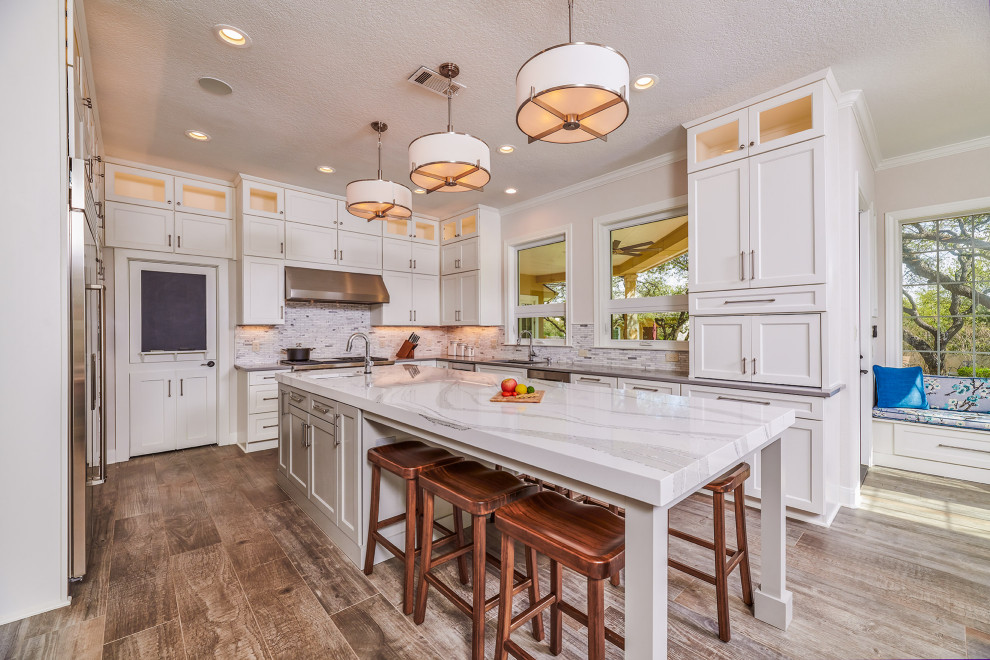 Kitchen - traditional brown floor kitchen idea in Austin with an undermount sink, shaker cabinets, white cabinets, gray backsplash, stainless steel appliances, an island and gray countertops