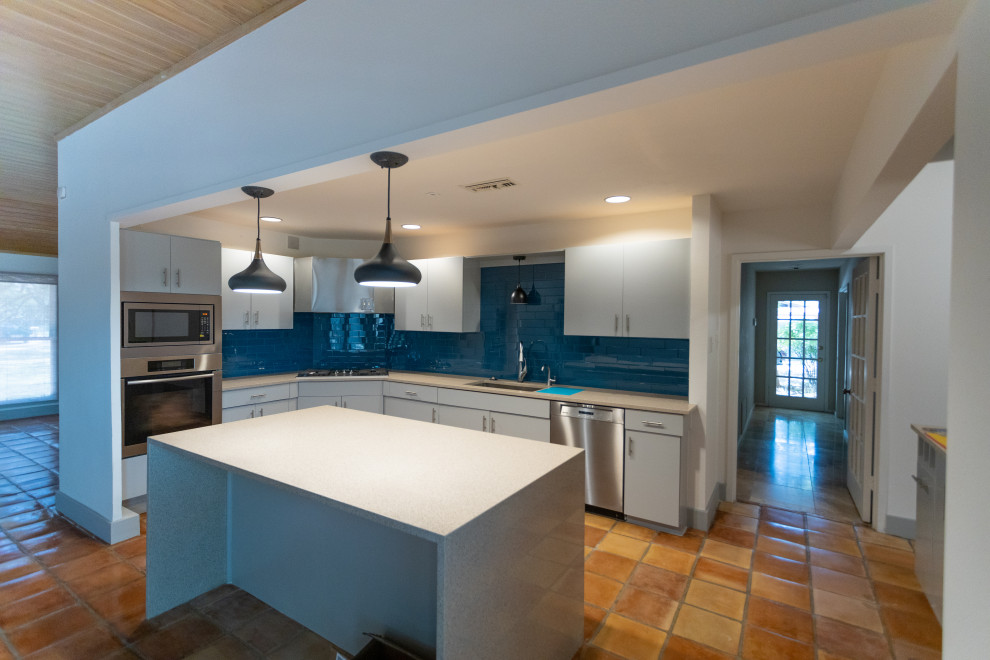 Foto på ett mellanstort beige kök, med en undermonterad diskho, släta luckor, grå skåp, bänkskiva i kvarts, blått stänkskydd, stänkskydd i glaskakel, rostfria vitvaror, klinkergolv i terrakotta, en köksö och brunt golv