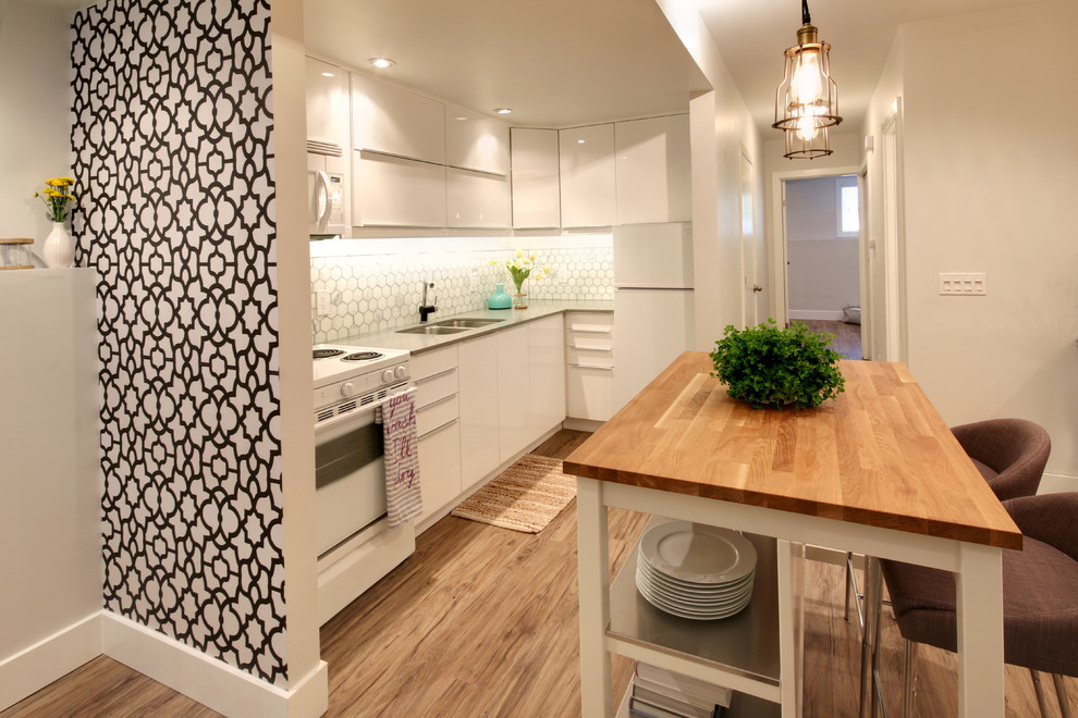 Inredning av ett modernt litet kök, med en undermonterad diskho, släta luckor, vita skåp, bänkskiva i kvarts, grått stänkskydd, stänkskydd i stenkakel, vita vitvaror, vinylgolv, en köksö och brunt golv
