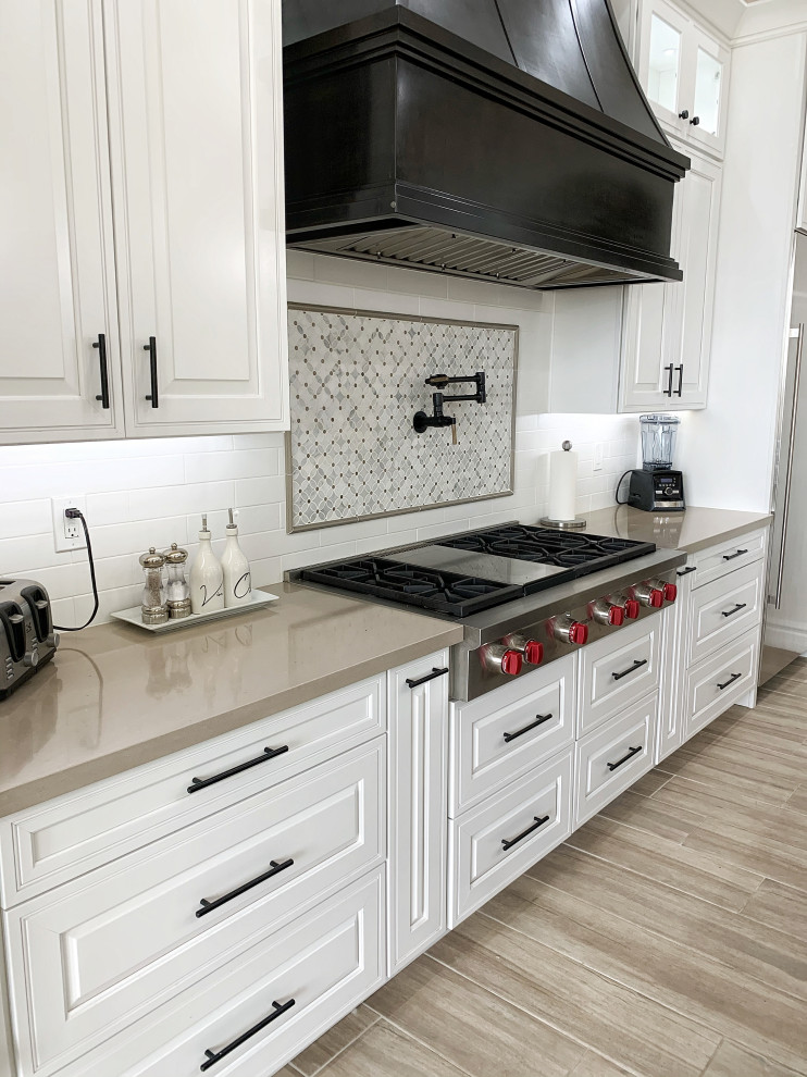 Example of a large transitional l-shaped cement tile floor and gray floor open concept kitchen design in Phoenix with a farmhouse sink, raised-panel cabinets, white cabinets, quartz countertops, white backsplash, ceramic backsplash, stainless steel appliances, an island and beige countertops