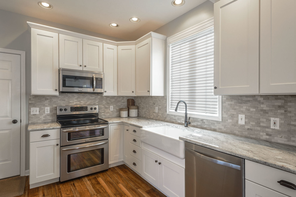 Mid-sized transitional l-shaped vinyl floor kitchen photo in Other with a farmhouse sink, an island, flat-panel cabinets, white cabinets, granite countertops, gray backsplash, stone tile backsplash and stainless steel appliances