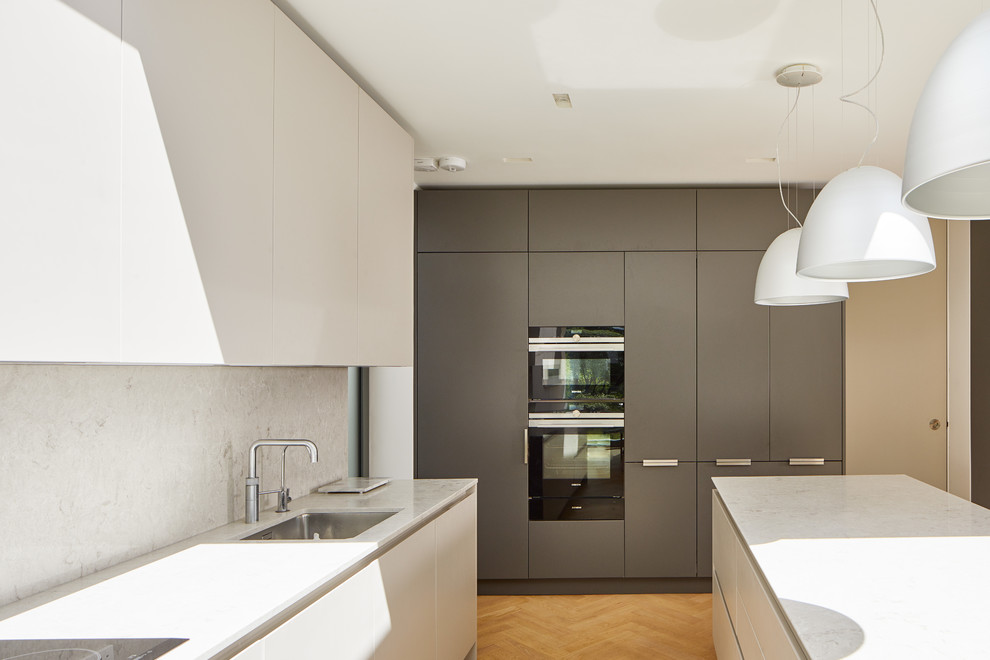 Moderne Küche mit Unterbauwaschbecken, flächenbündigen Schrankfronten, weißen Schränken, braunem Holzboden, Kücheninsel, braunem Boden und weißer Arbeitsplatte in London