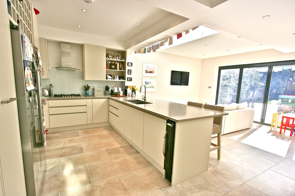 Medium sized contemporary u-shaped open plan kitchen in London with a double-bowl sink, flat-panel cabinets, beige cabinets, composite countertops, white splashback, glass sheet splashback, integrated appliances, travertine flooring and a breakfast bar.