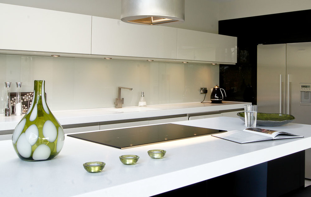 This is an example of a large contemporary open plan kitchen in Manchester with a submerged sink, flat-panel cabinets, white cabinets, composite countertops, glass sheet splashback, stainless steel appliances, porcelain flooring and an island.