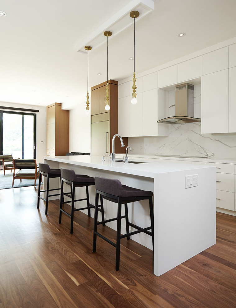 This is an example of a contemporary galley kitchen in Toronto with a submerged sink, flat-panel cabinets, white cabinets, white splashback, stone slab splashback, integrated appliances, dark hardwood flooring and an island.