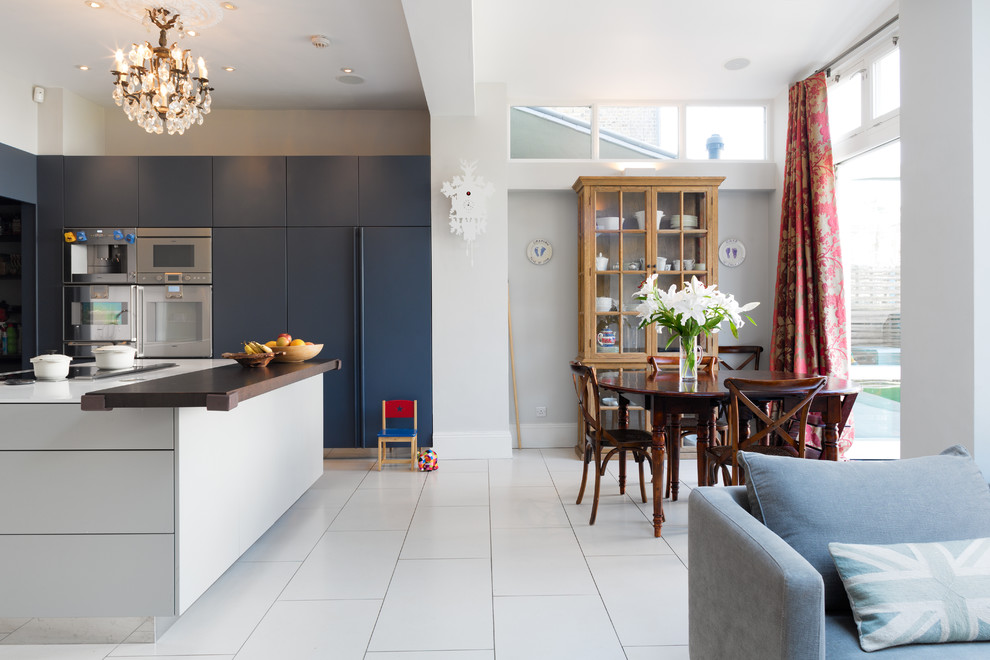 Photo of a contemporary l-shaped kitchen/diner in London with flat-panel cabinets, blue cabinets, an island, a built-in sink, integrated appliances and wood worktops.