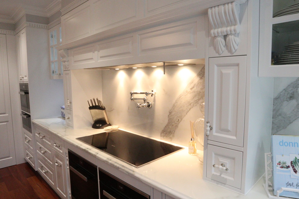 Klassisk inredning av ett stort kök, med en rustik diskho, luckor med profilerade fronter, vita skåp, marmorbänkskiva, vitt stänkskydd, stänkskydd i marmor, svarta vitvaror, mellanmörkt trägolv, en köksö och brunt golv