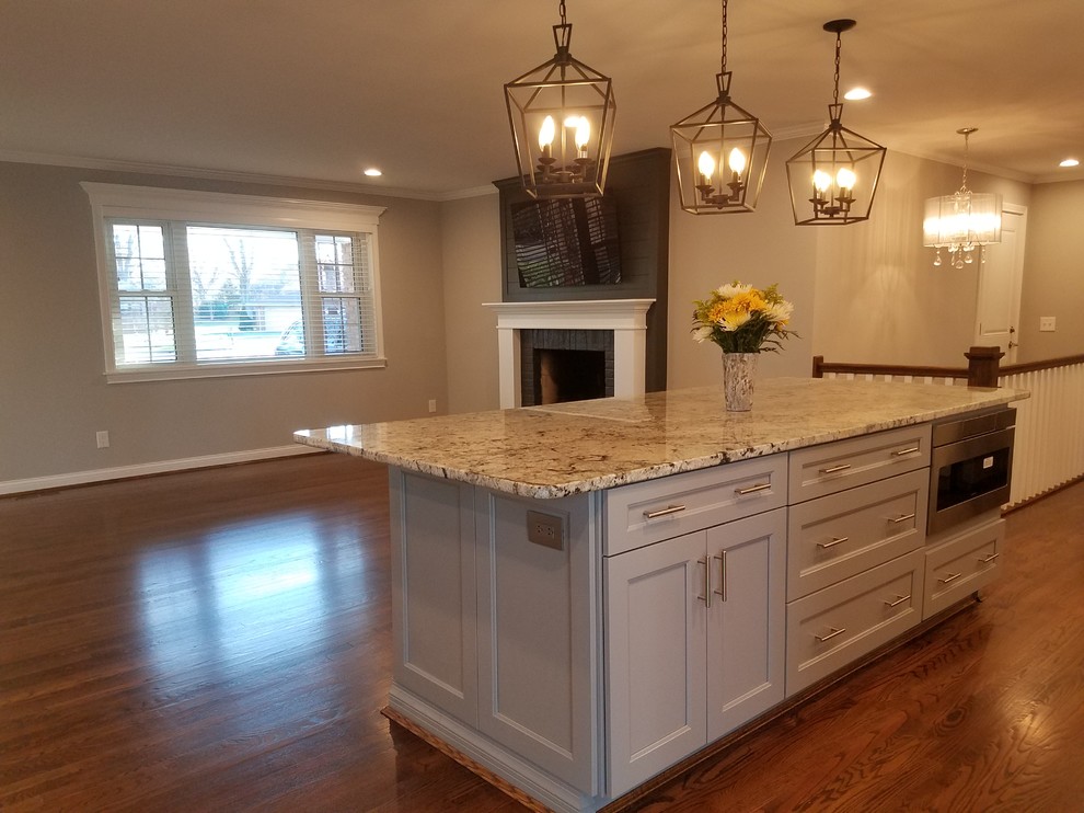 Inspiration for a mid-sized craftsman single-wall medium tone wood floor and brown floor open concept kitchen remodel in Cincinnati with an undermount sink, shaker cabinets, white cabinets, granite countertops, gray backsplash, glass tile backsplash, stainless steel appliances and an island