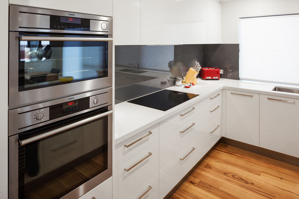 Foto på ett funkis vit kök, med släta luckor, vita skåp, bänkskiva i kvarts, svart stänkskydd, glaspanel som stänkskydd och svarta vitvaror