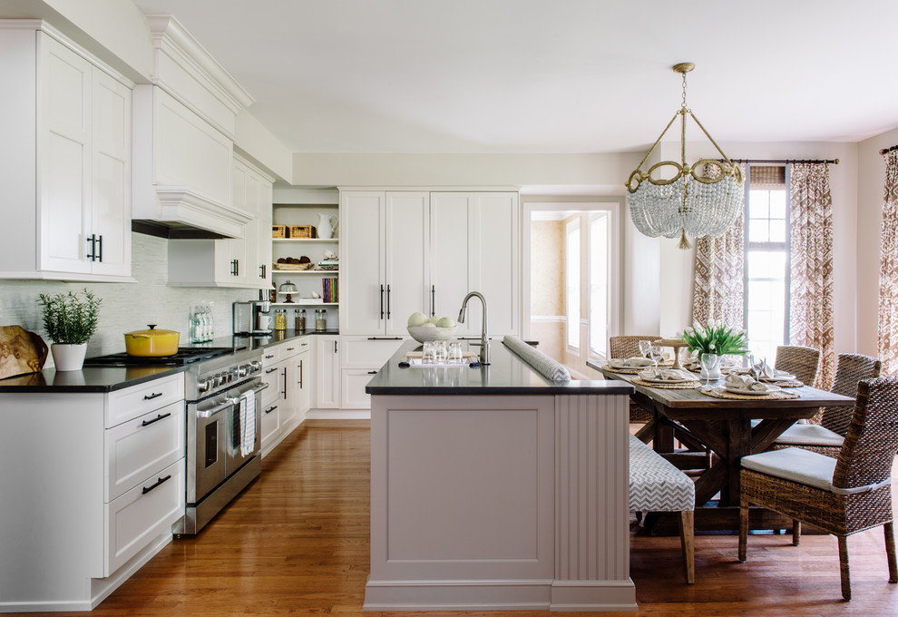 This is an example of a classic galley kitchen/diner in DC Metro with white cabinets, composite countertops, grey splashback, stainless steel appliances, medium hardwood flooring and an island.