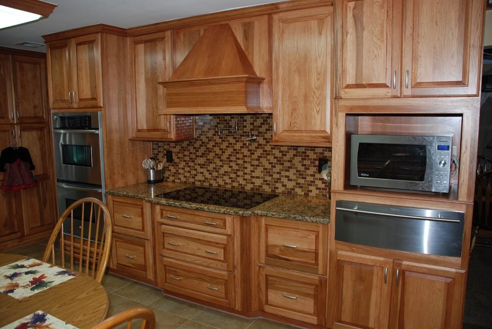 Example of a mid-sized mountain style l-shaped ceramic tile eat-in kitchen design in Raleigh with an undermount sink, raised-panel cabinets, granite countertops, brown backsplash, glass tile backsplash, stainless steel appliances and a peninsula