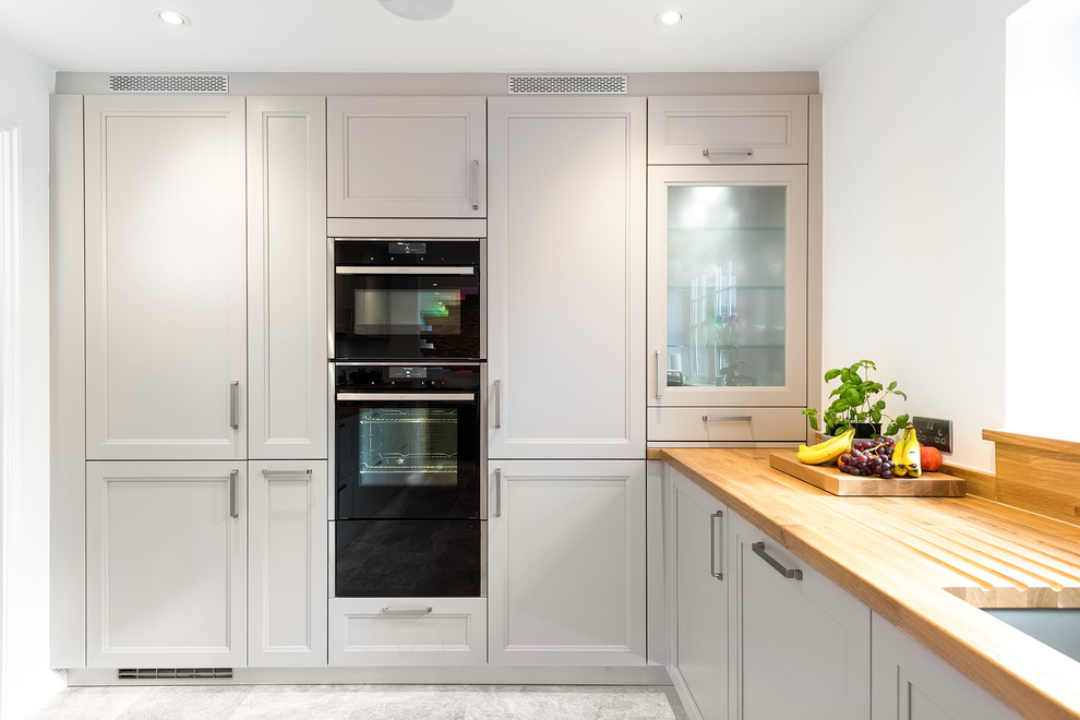 Example of a mid-sized classic travertine floor eat-in kitchen design in Buckinghamshire with a double-bowl sink, shaker cabinets, gray cabinets, wood countertops and stainless steel appliances
