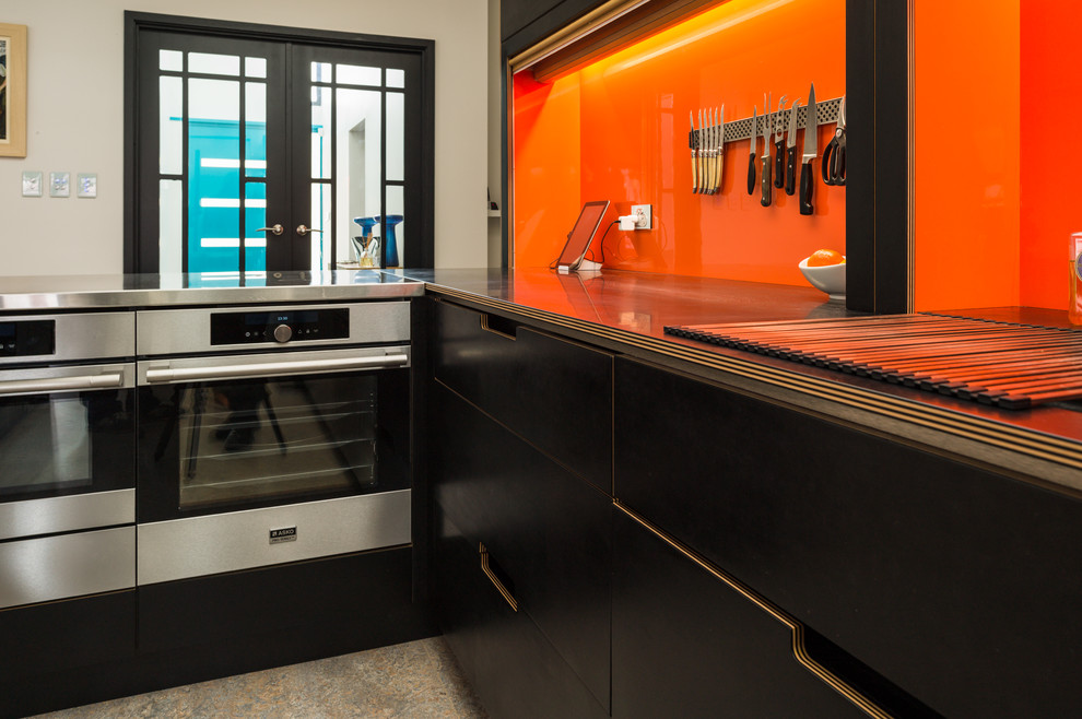 Immagine di una grande cucina minimal con lavello a doppia vasca, ante lisce, ante nere, paraspruzzi arancione, elettrodomestici in acciaio inossidabile, pavimento in linoleum e top nero
