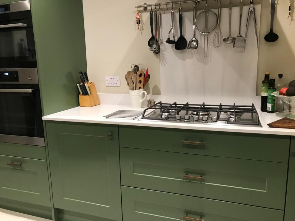 Mid-sized minimalist white floor kitchen photo in London with green cabinets, white backsplash and white countertops