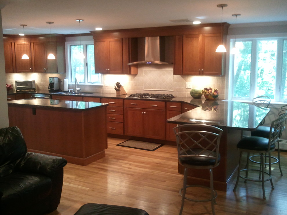 Example of a classic u-shaped light wood floor eat-in kitchen design in Boston with an undermount sink, shaker cabinets, dark wood cabinets, granite countertops, beige backsplash, travertine backsplash, stainless steel appliances, an island and black countertops