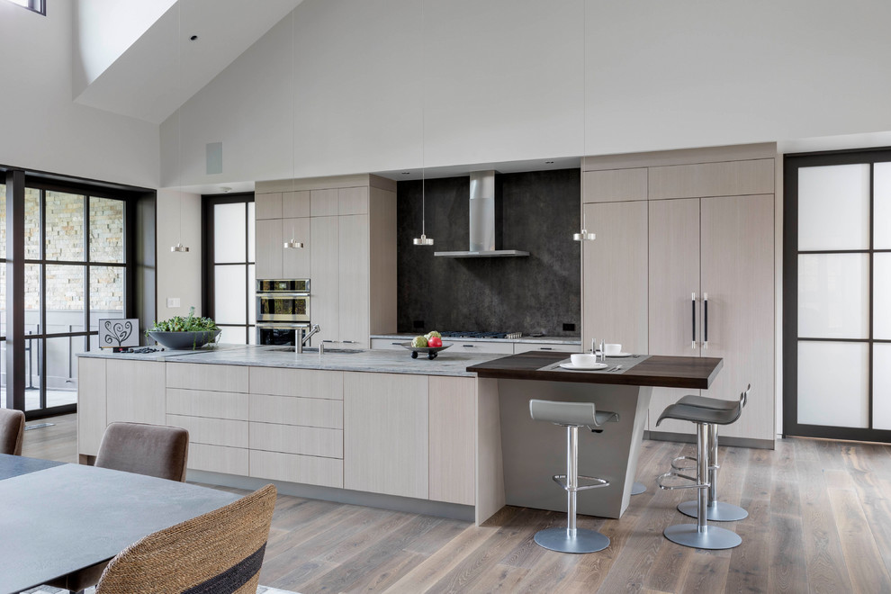 Modern inredning av ett grå grått kök, med en undermonterad diskho, släta luckor, skåp i ljust trä, grått stänkskydd, integrerade vitvaror, mellanmörkt trägolv, en köksö och brunt golv